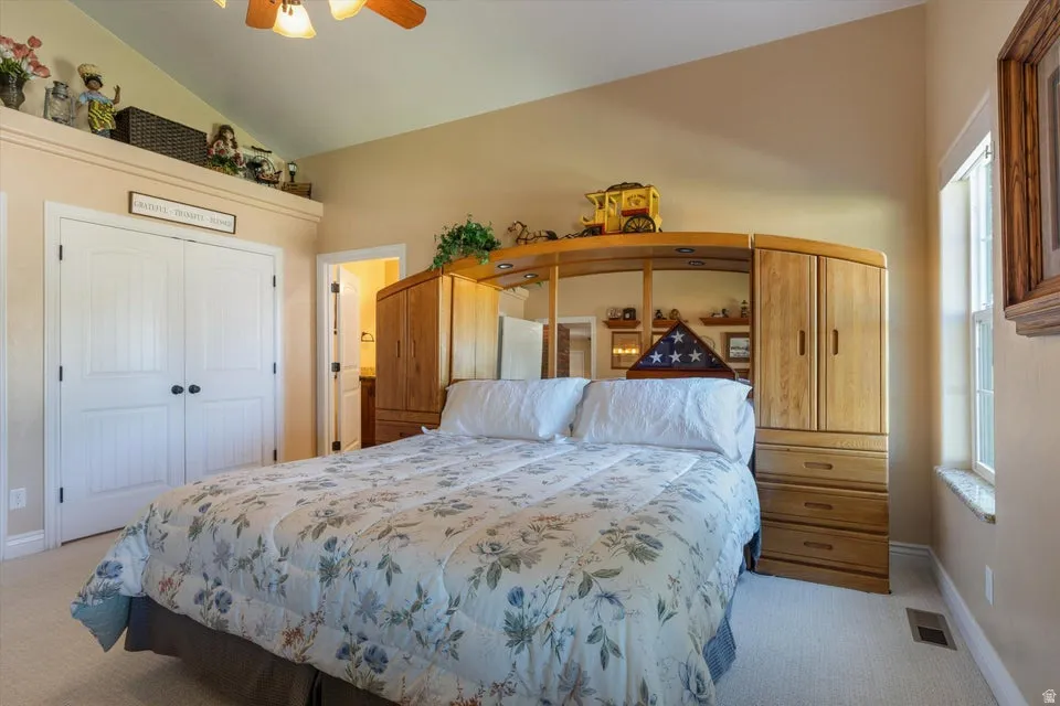 Vaulted ceiling with a ceiling fan, light-colored carpeting, white double bi-fold closet doors, and a window with a stone sill