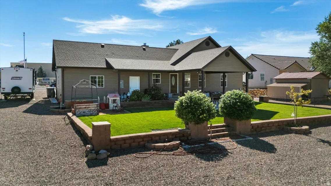 Gable-roof property featuring a covered front porch, gravel driveway, and a retaining wall with a manicured lawn