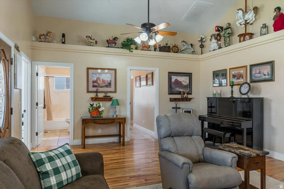 Vaulted ceiling with a ceiling fan, wood-finish flooring, and a decorative ledge