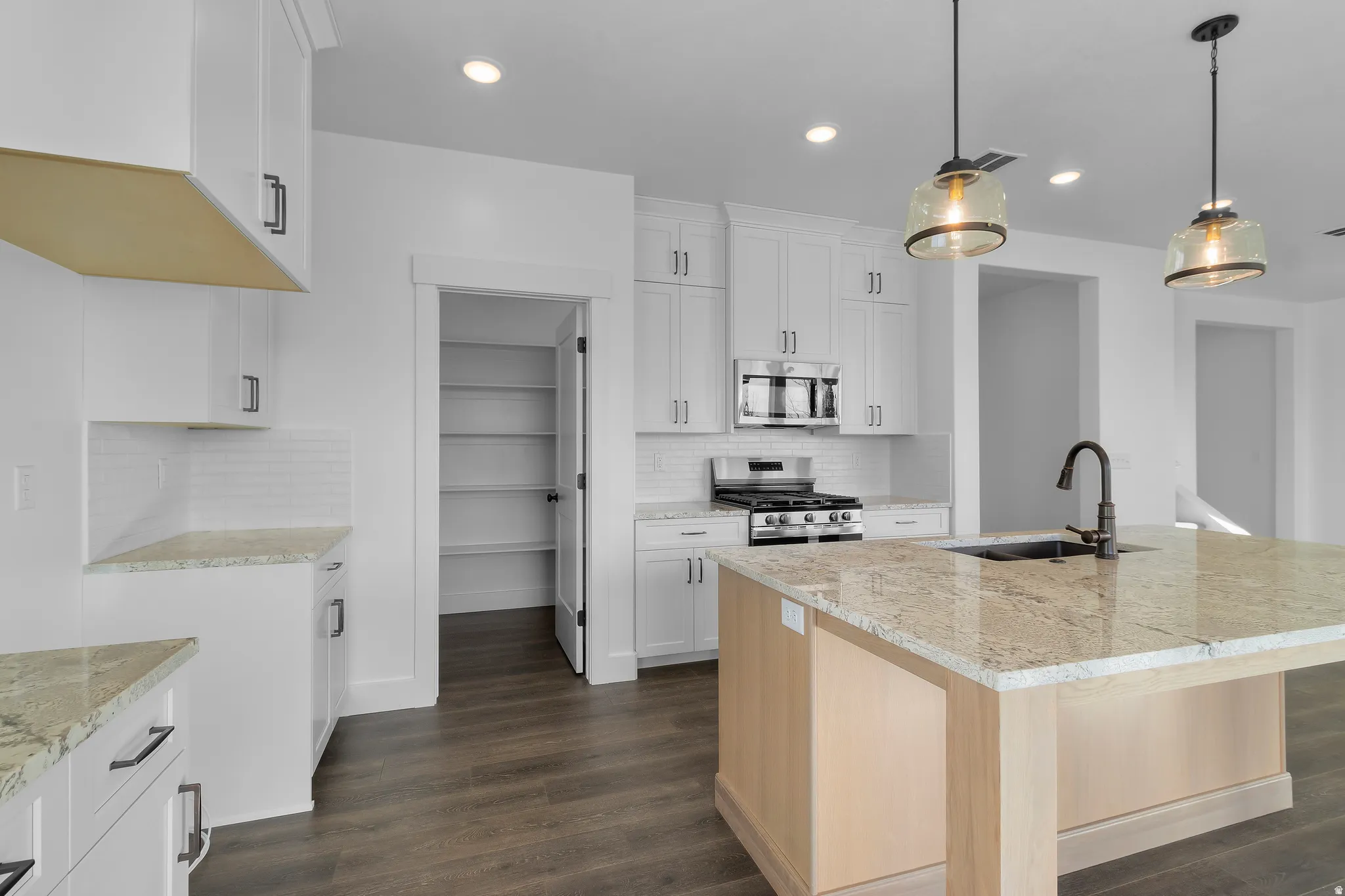 Kitchen featuring an island with stone countertop and sink, white cabinetry, stainless steel appliances, and wood-finish flooring