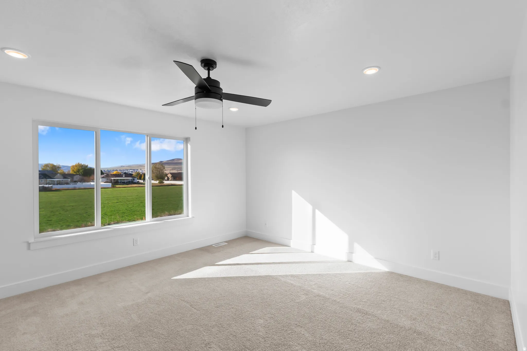 Expansive window providing abundant natural light, neutral carpet, recessed lighting, and a ceiling fan