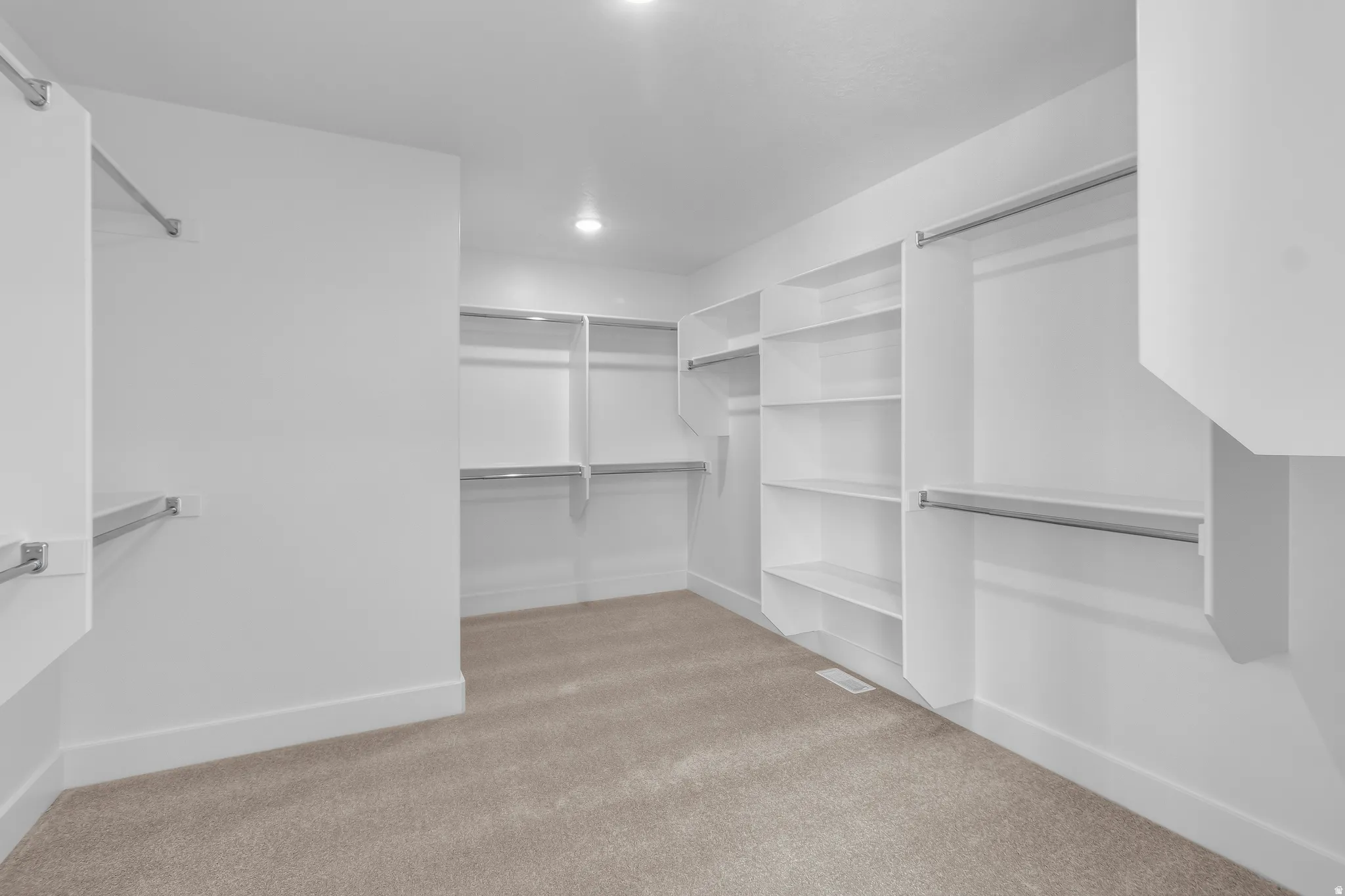Recessed lighting illuminates the organized closet space featuring built-in shelving, hanging rods, and carpet flooring