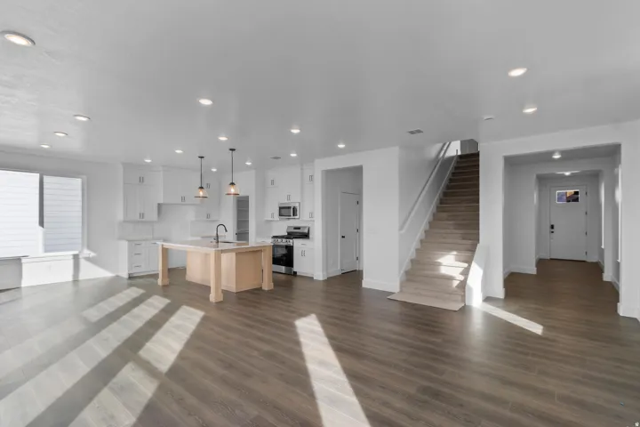 Open-concept living space featuring wood-finish flooring, recessed lighting, and a kitchen with white cabinetry and a central island