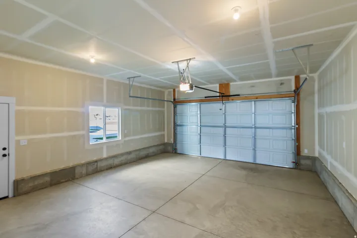 Spacious garage featuring a concrete floor, overhead lighting, an automatic garage door opener, and a window for natural light