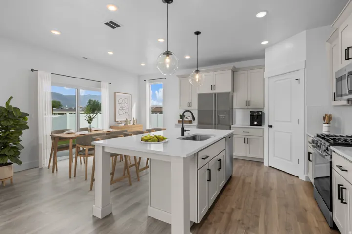 Kitchen with wood-finish flooring, white cabinetry, a center island with sink, stainless steel appliances, and recessed lighting