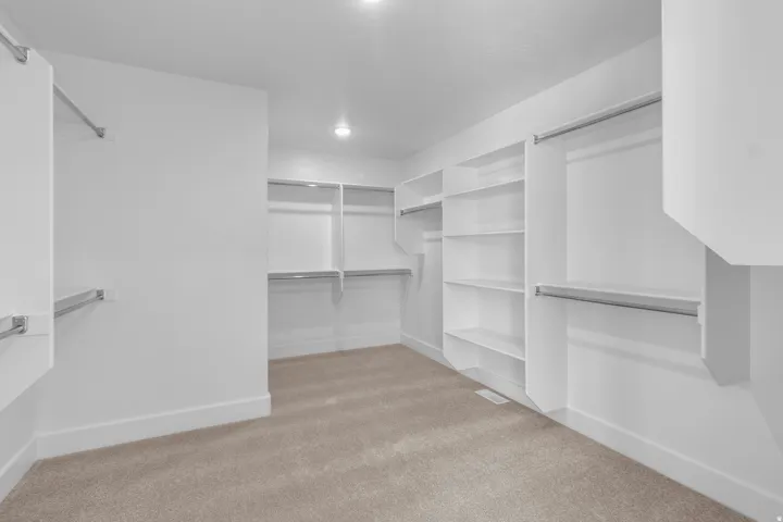 Recessed lighting illuminates the organized closet space featuring built-in shelving, hanging rods, and carpet flooring