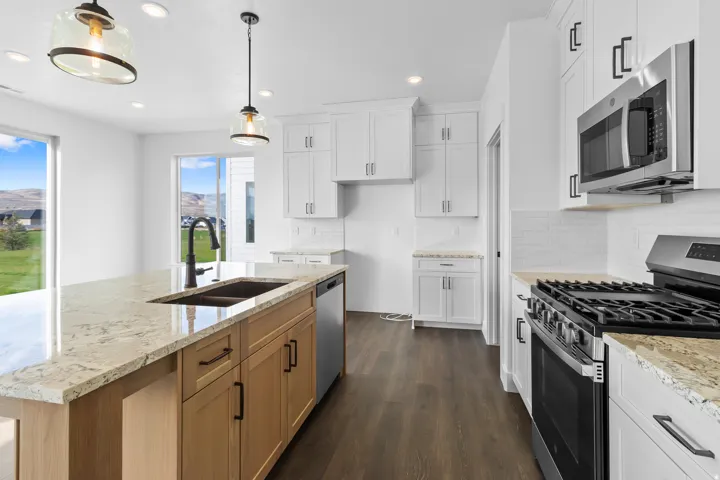 Kitchen featuring a large island with an undermount sink, granite countertops, wood-finish flooring, white cabinetry, and stainless steel appliances