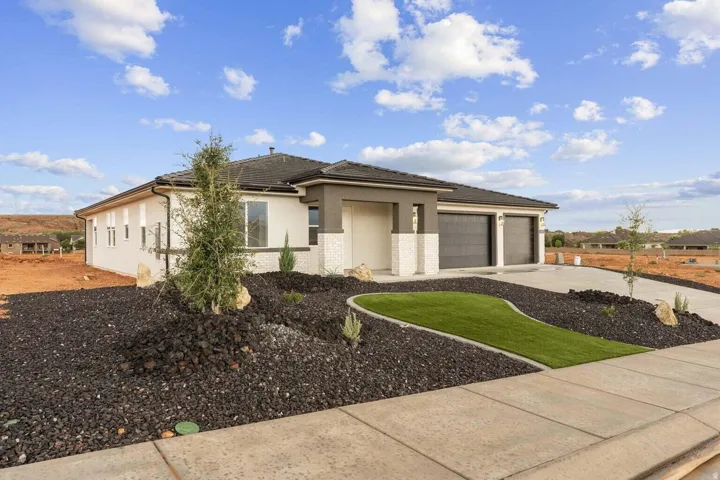 Contemporary stucco exterior, stone accent detailing, two-car garage, concrete driveway, and low-maintenance landscaping with artificial turf