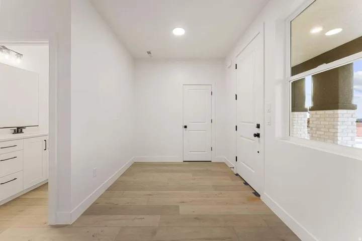 Wood-finish flooring, recessed lighting, white interior doors with black hardware, and a window with exterior stone and column details