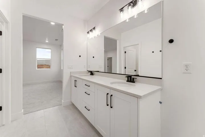 Double vanity with white cabinetry, integrated sinks, black hardware, and an expansive mirror