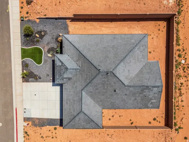 Pitched roof with dark gray shingles, concrete perimeter fencing, and a concrete driveway