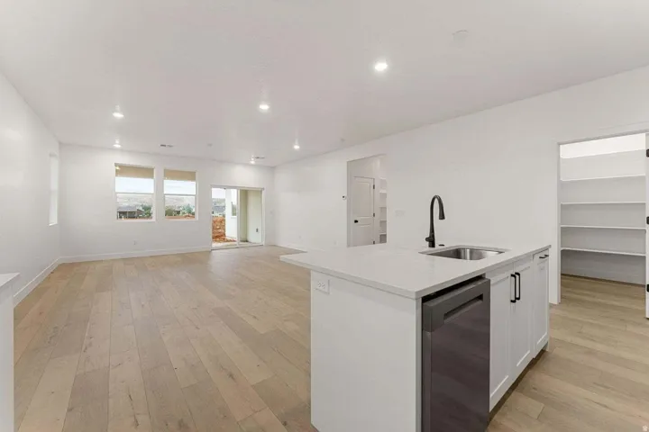 Open-concept living space with light wood-finish flooring, recessed lighting, and a kitchen island featuring a stainless steel sink, matte black faucet, and dishwasher