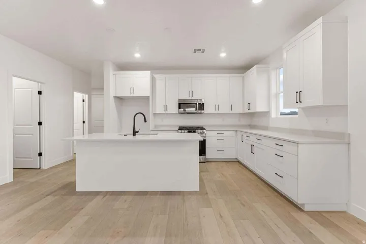 Kitchen featuring white shaker cabinetry, an island with an integrated sink, light-toned wood-finish flooring, stainless steel appliances, and recessed lighting