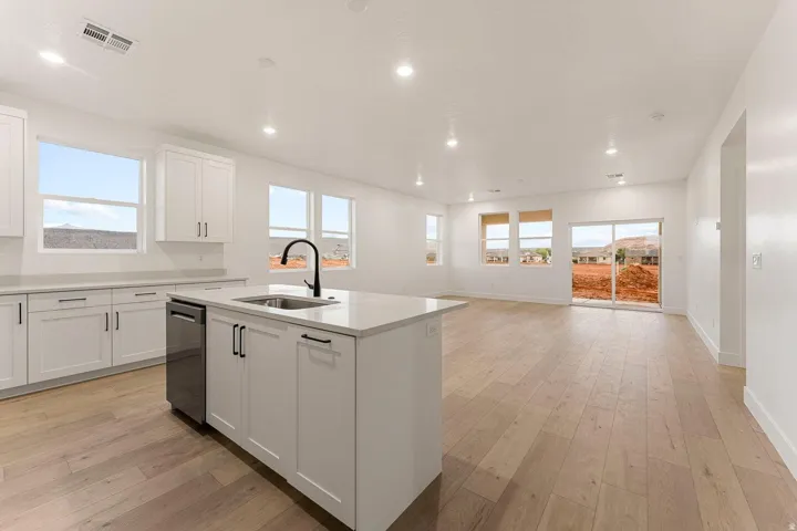 Contemporary kitchen featuring white cabinetry, a large center island with a sink and black faucet, a built-in dishwasher, and wood-finish flooring