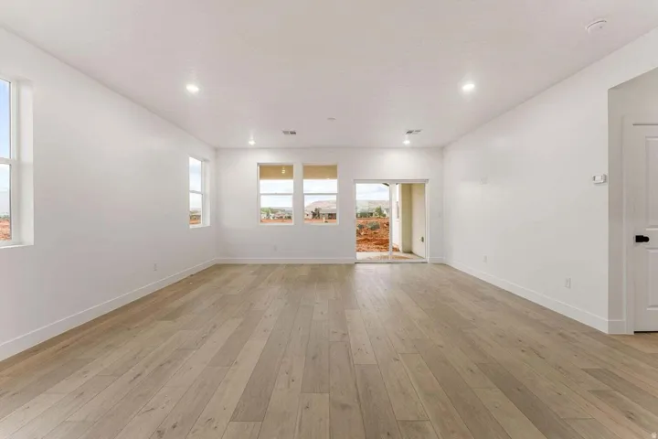 Expansive room with light wood-finish flooring, recessed lighting, multiple windows, and a sliding glass door