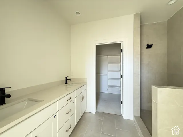 Dual undermount sinks with matte black faucets, extended vanity with quartz countertop, light-toned floor tile, and a walk-in shower with tiled walls
