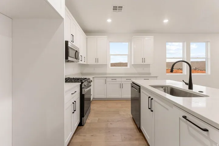 White cabinetry, light wood-finish flooring, stainless steel appliances, white countertops, and recessed lighting