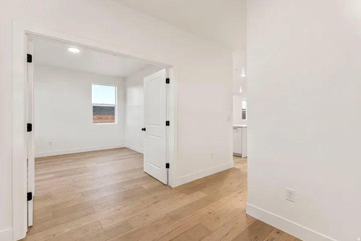 Light wood-finish flooring throughout, white walls, recessed ceiling lighting, and a single window with a dark frame