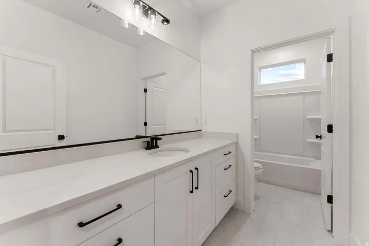 Expansive vanity with a single basin, light-toned countertop, and white cabinetry featuring matte black hardware