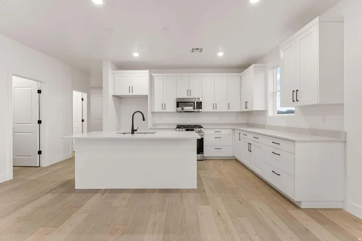 Contemporary kitchen with white shaker cabinetry, stainless steel appliances, and a central island with a matte black faucet