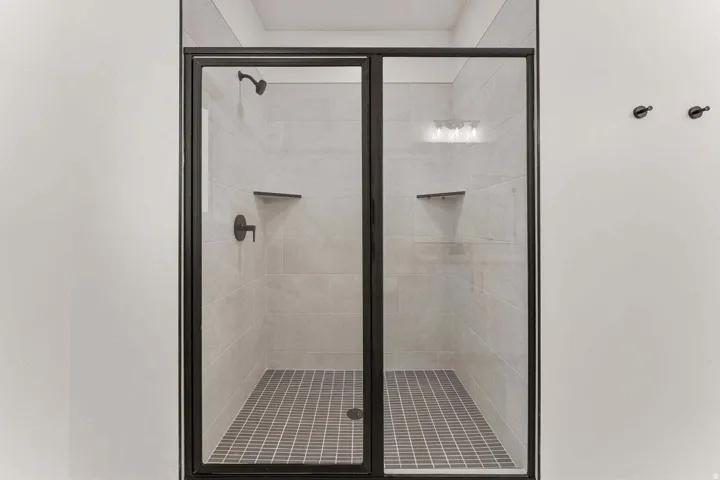 Shower enclosure with matte black framing, light-toned wall tile, and gray mosaic floor tile
