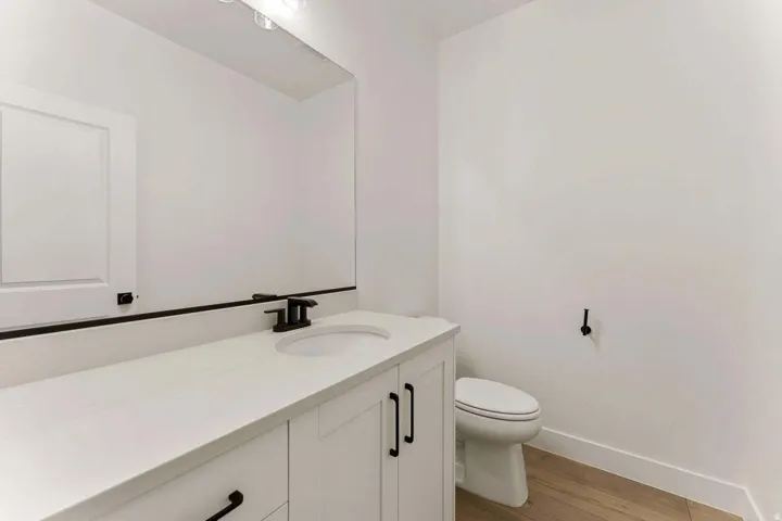 White cabinetry with matte black hardware, integrated sink, and wood-finish flooring