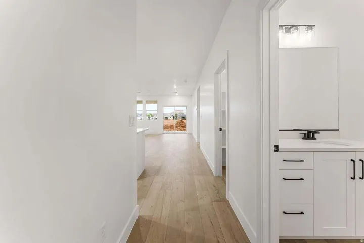 Wood-finish flooring throughout, white shaker-style vanity with matte black hardware, integrated sink, and wall-mounted mirror