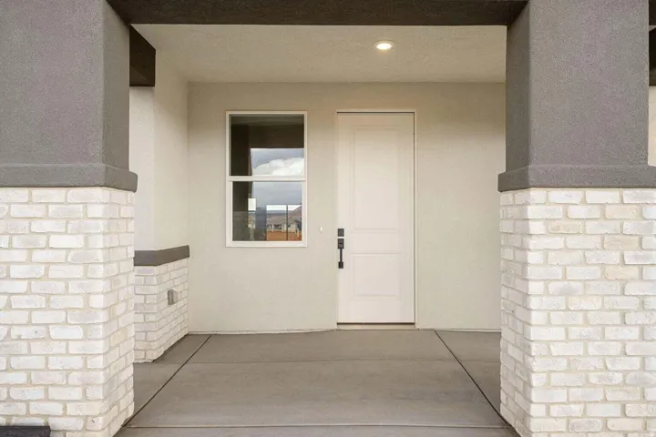 Covered entryway featuring a single-panel door with black hardware, recessed lighting, and a neutral stucco finish