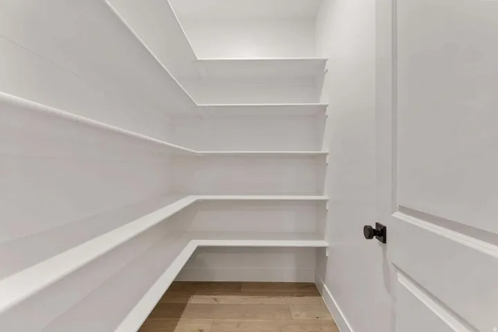 Integrated wall-mounted shelving with white finish, wood-finish flooring, and a white paneled door with a black knob