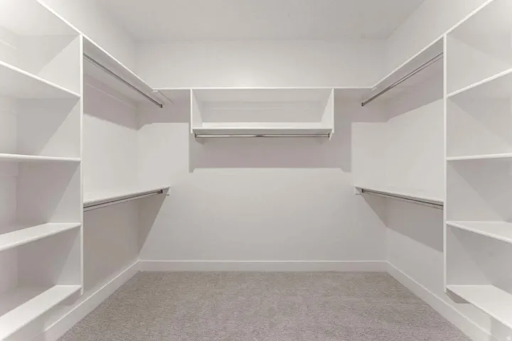 Built-in shelving with multiple storage levels, integrated hanging rods, and light gray carpeting