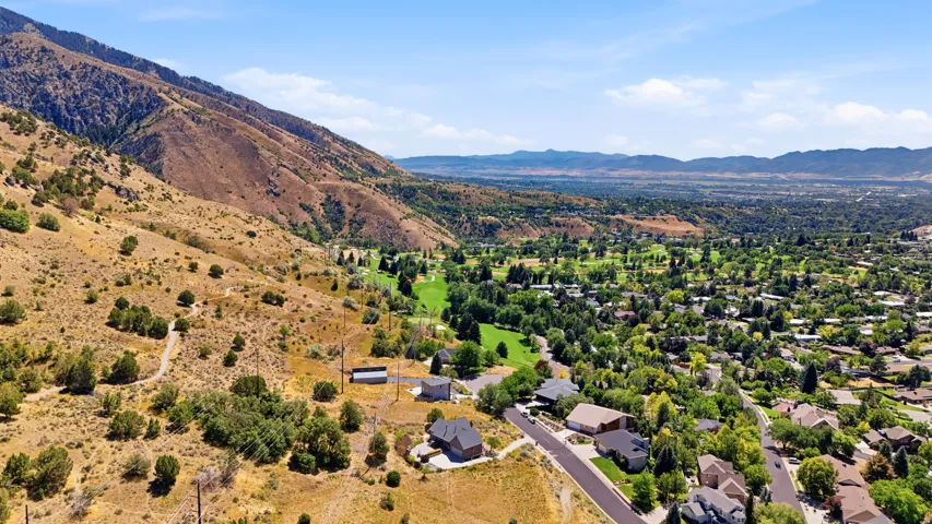 Mountainous terrain, residential properties, distant valley, green spaces, clear sky