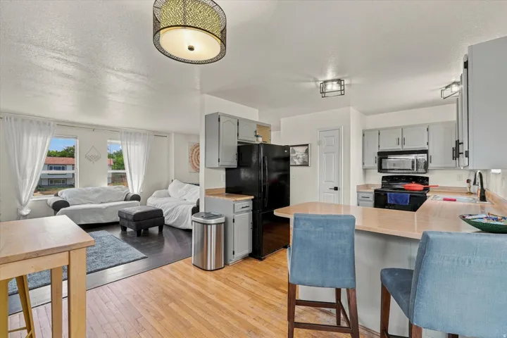 Open-concept living area featuring a kitchen with gray cabinetry, black appliances, and a breakfast bar, complemented by wood-finish flooring