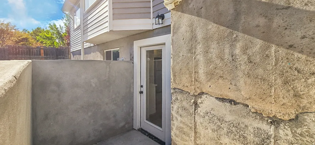 Siding exterior with a ground-level entry door, exterior wall sconce, and concrete retaining walls