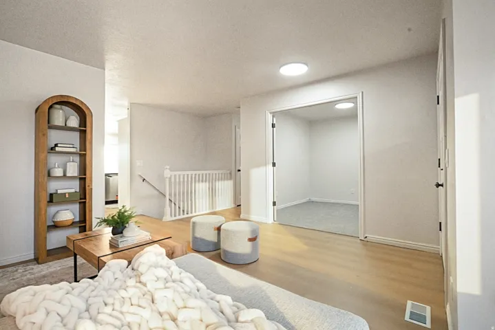 Wood-finish flooring, staircase with white railing, built-in wooden shelving unit, recessed lighting, and a separate room with carpeting