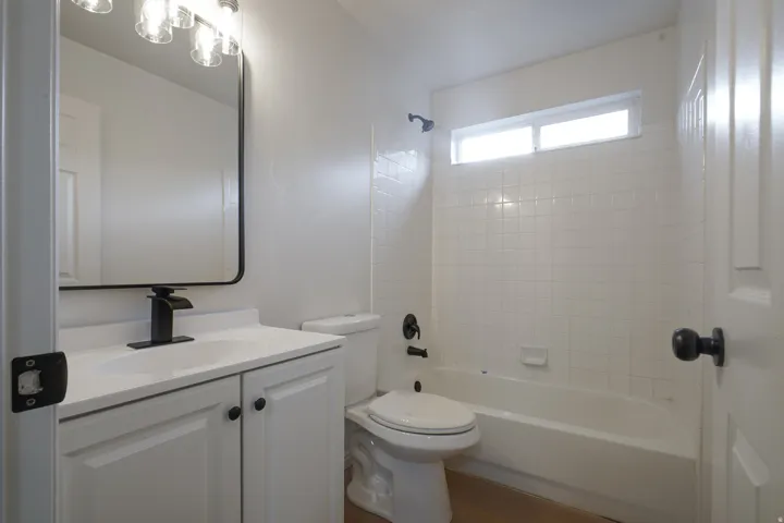 Bathroom featuring a white vanity with integrated sink, black fixtures, and a tiled tub shower with a transom window