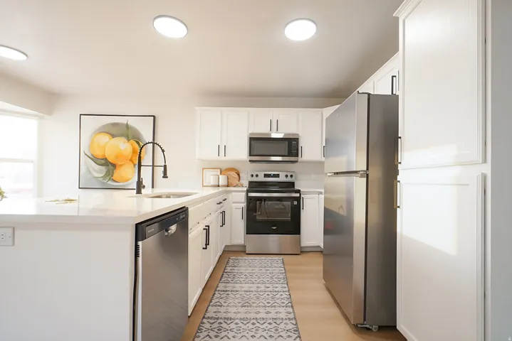 Modern kitchen featuring white cabinetry, stainless steel appliances, a kitchen island with sink, and light wood-finish flooring