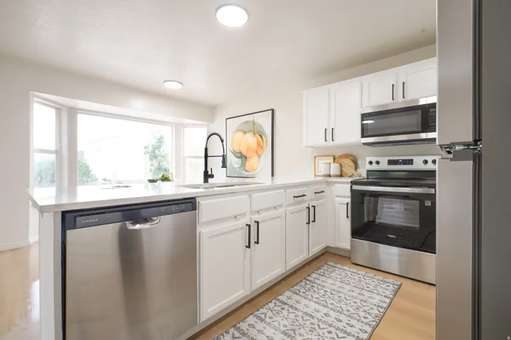White cabinetry with matte black hardware, stainless steel appliances, light-toned wood-finish flooring, recessed lighting, and a bay window