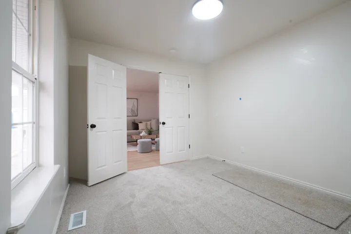 Plush carpeting, paneled double doors, window with horizontal blinds, overhead flush mount lighting, and neutral wall finishes