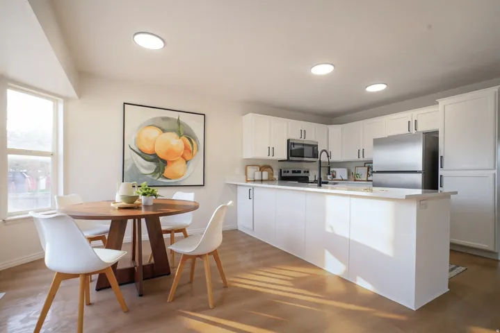 Open-concept kitchen with white cabinetry, stainless steel appliances, a central island, and wood-finish flooring