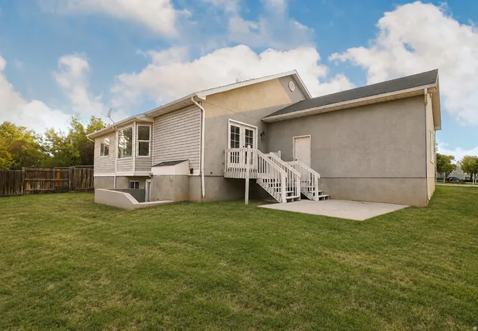Expansive backyard featuring a concrete patio, wooden deck with stairs, and a bay window
