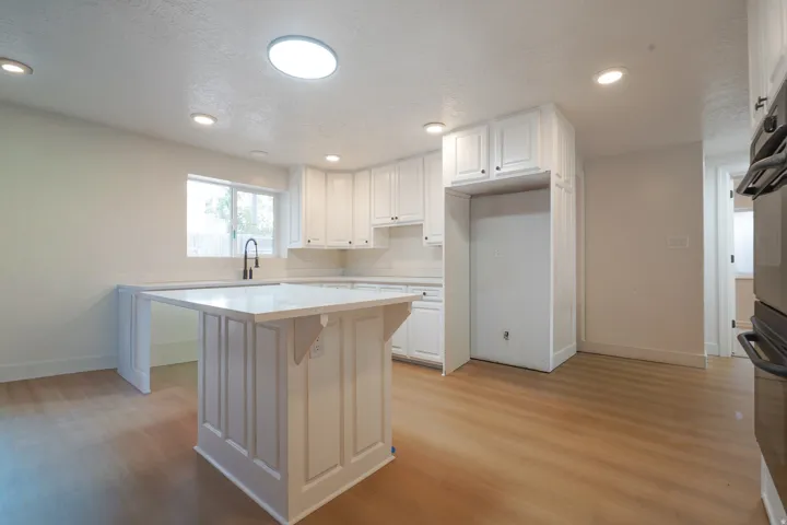 White cabinetry, wood-finish flooring, recessed lighting, and a kitchen island with a white countertop