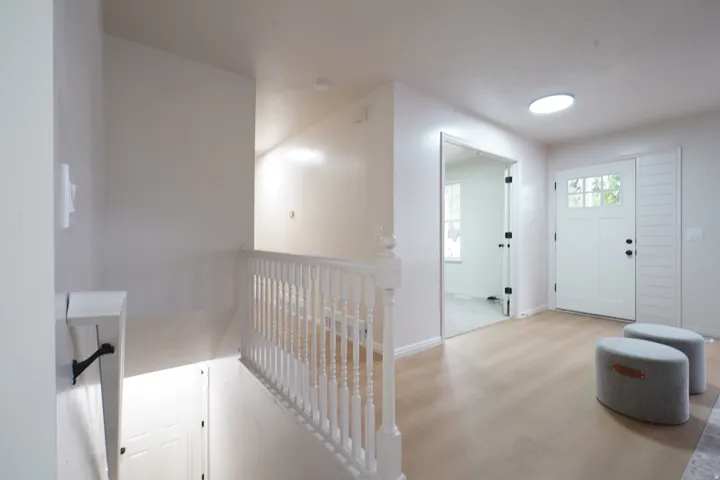 Light wood-finish flooring, white spindle railing, paneled front door with windowpanes, modern cylindrical ceiling light, and a clear glass interior door
