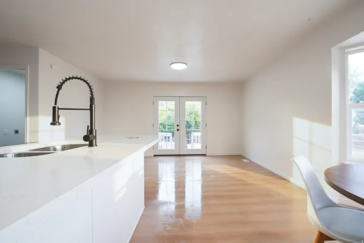 Kitchen island with integrated double basin sink, modern black gooseneck faucet, light-toned countertops, and wood-finish flooring