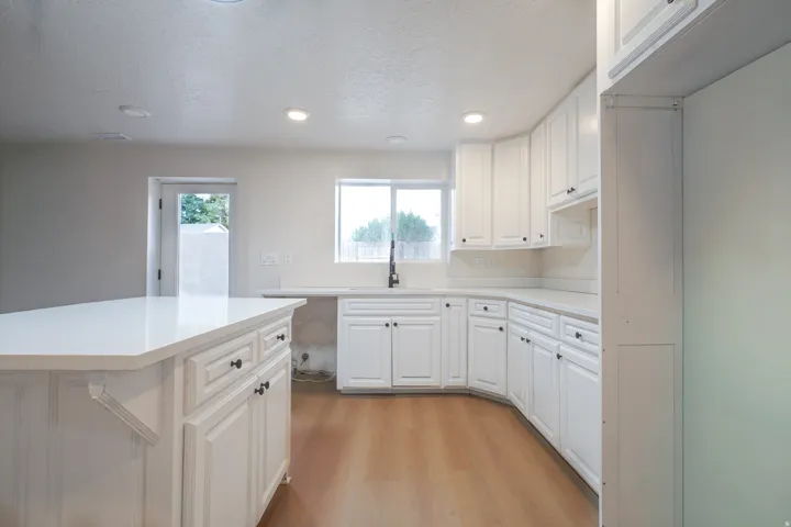 Kitchen with wood-finish flooring, white cabinetry, recessed lighting, and a white countertop island