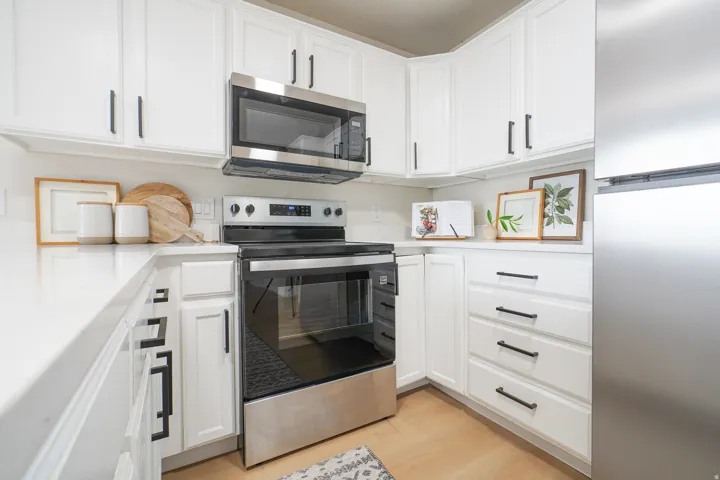 White cabinetry with modern black hardware, stainless steel appliances, light-toned countertops, and wood-finish flooring