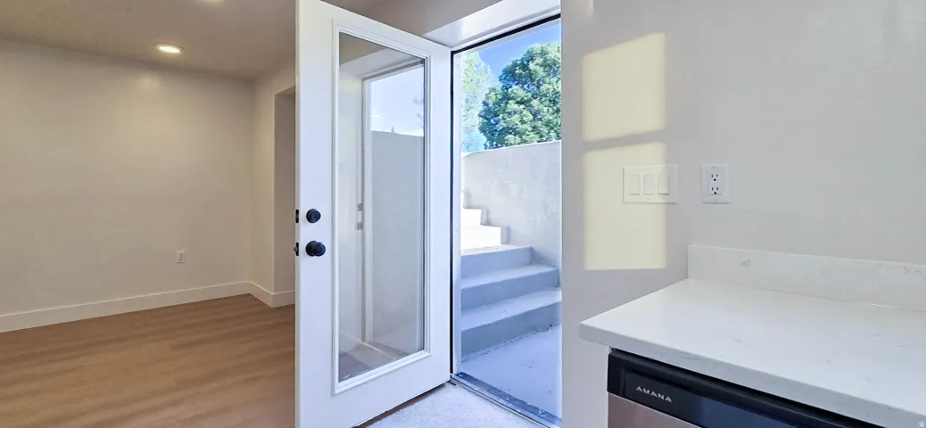 Glass-panel door leading to an outdoor staircase, white countertop with an under-counter appliance, wood-finish flooring, and recessed lighting