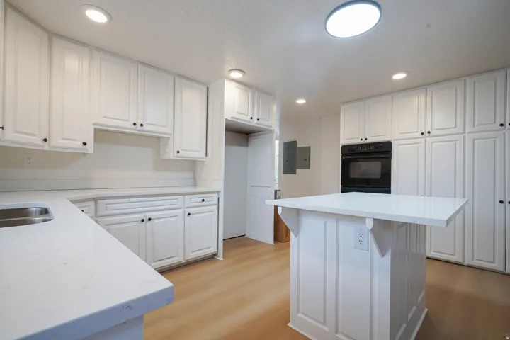 White cabinetry with black hardware, stone countertops, wood-finish flooring, and a built-in oven