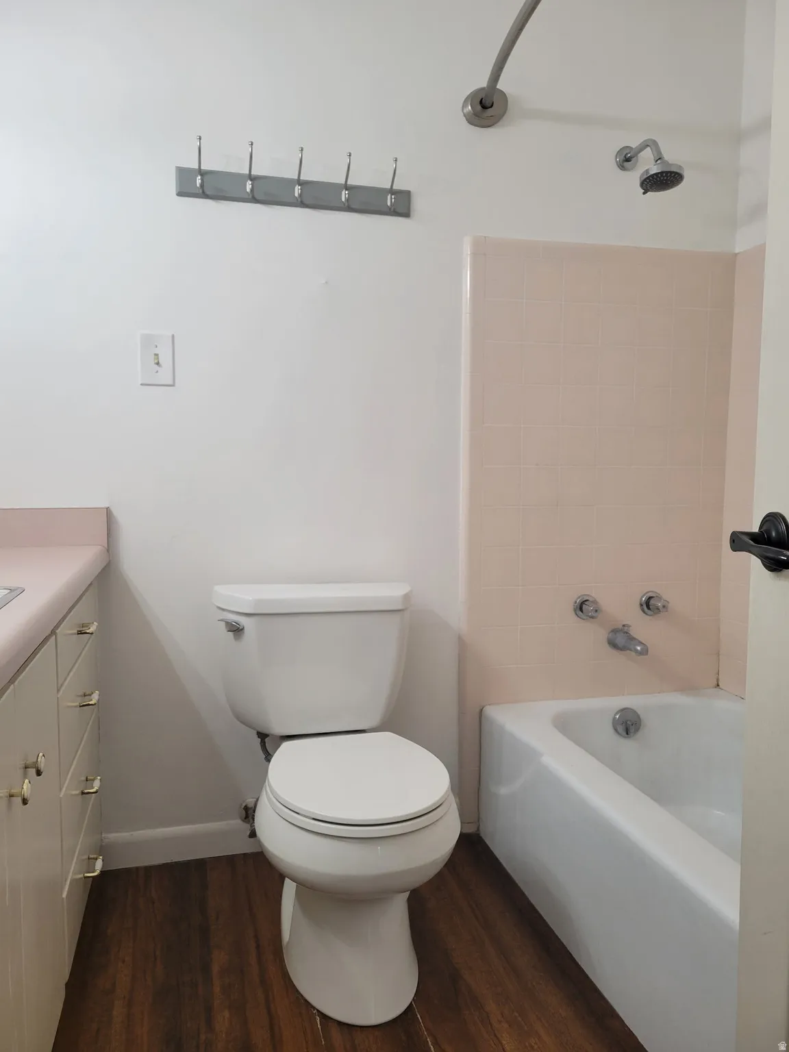 Built-in bathtub with shower fixture, white toilet, vanity with light-colored countertop, and wood-finish flooring
