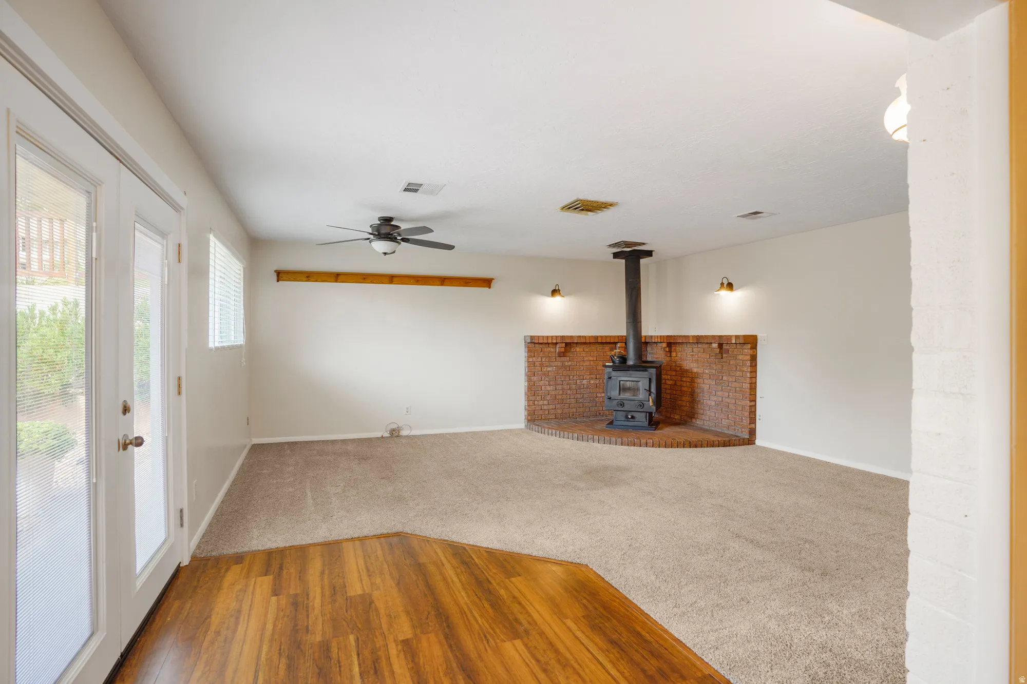 Wood-finish flooring at entry, leading to a carpeted living area with a ceiling fan