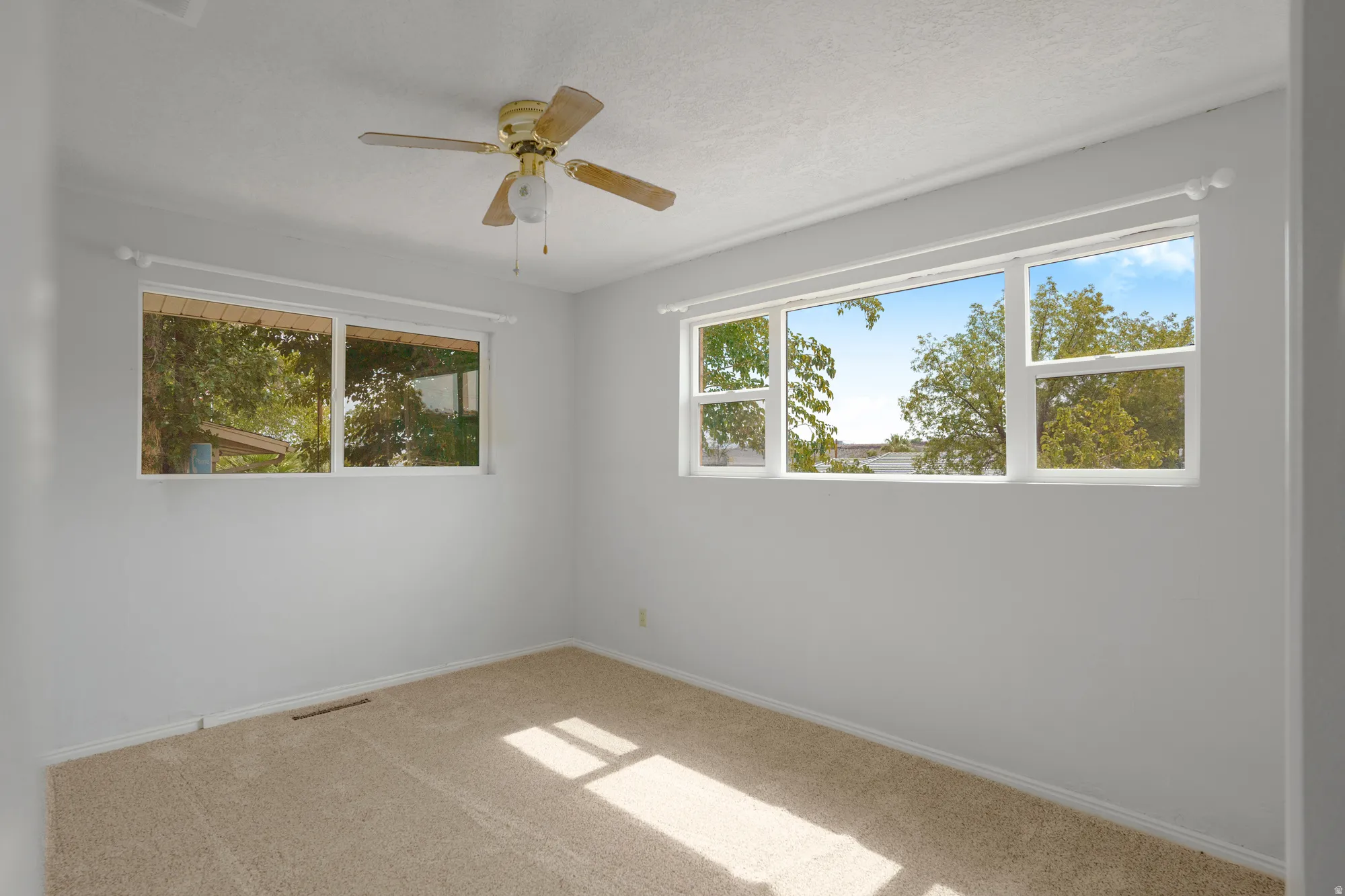Neutral wall paint, ceiling fan with light fixture, two multi-pane windows, and carpeted flooring